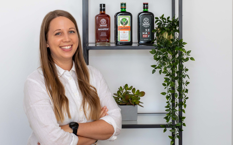 Nina Reissner vor einem Regal mit 3 Jägermeister-Varianten