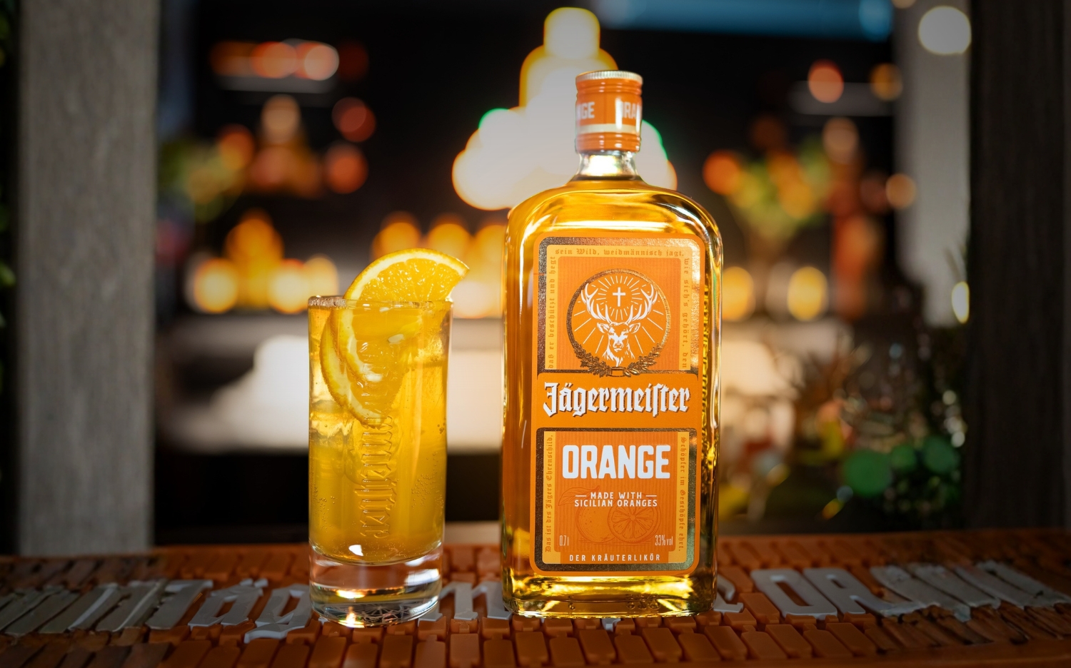 Eine Flasche Jägermeister Orange steht neben einem vollen Glas mit Orangenscheibe auf einer Bar